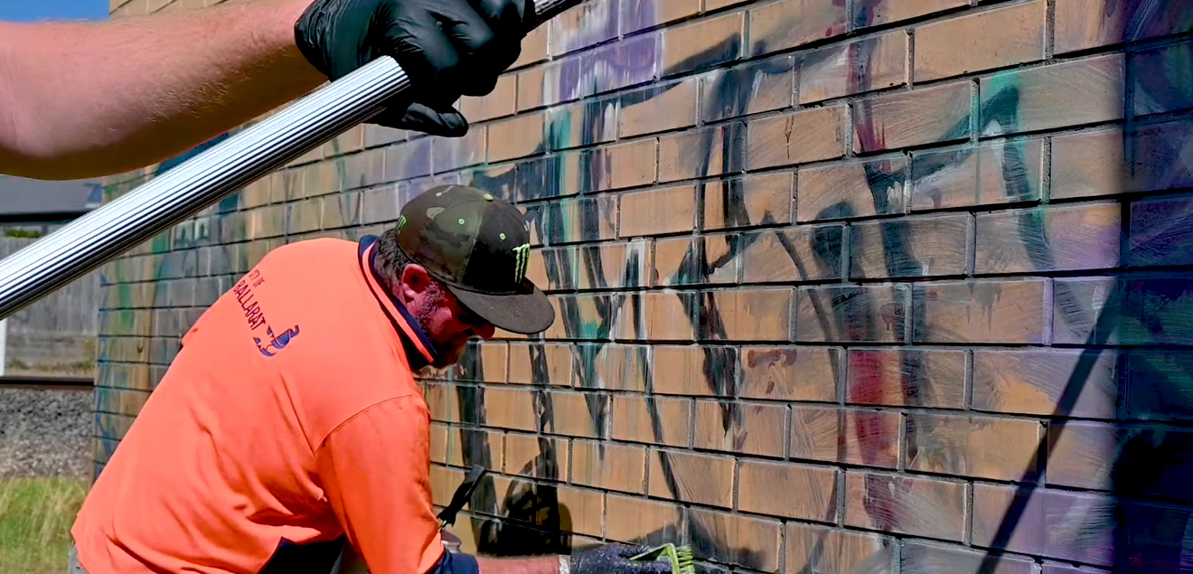 Mens in high viz removing graffiti from brick wall.